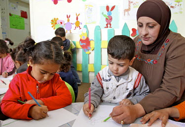 A teacher helps children in an art class. The Ramtha facility has been opened by the Government of Jordan to receive Syrian refugees. UNICEF is providing psycho-social support for the children in the...