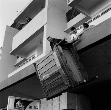 Three men struggle to raise a large wardrobe to the first floor balcony at the Lambis Centre on Prince George Avenue.