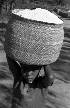 A young girl carries an Iringa basket filled with freshly milled flour.