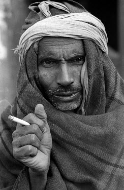 A man, wrapped up against the cold, smokes a cigarette.