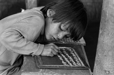 A young pupil, studying in a village school, writes on a small board with a piece of chalk.