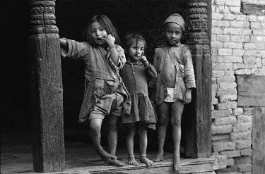 Three young children standing on the veranda of a building.