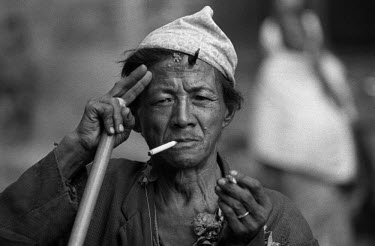 A man with a cigarette in his hand and another in his mouth. He has a tikalteeka, a mixture of abir (red powder dye), yoghurt and grains of rice applied by a priest as a blessing, on his forehead.