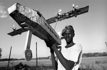 A Dinka boy, living in the Kakuma Refugee Camp, holds aloft his model of a Russian Antonov cargo plane made from scraps of wood and metal.