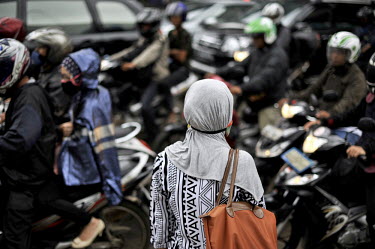 A young woman in muslim headdress and with pollution mask waits for a break in the traffic to cross a typical section of road in Jakarta. With 10-plus million people living in the capital - 25 million...