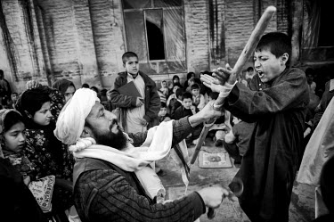 A child cries out as he is punished at a religious school by a man who has tied the boy to a stick.