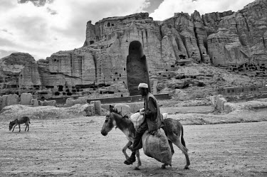 A man rides his donkey past the remnants of the Bamiyan Buddhas, destroyed by the Taliban in March 2001. While the limited efforts to rebuild them have had negligible success some 2000 caves in the ar...