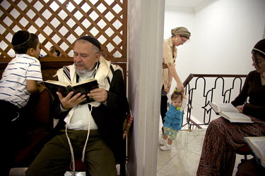 A man reads from a prayer book while a mother cares for her daughter during prayers in the synagogue. They belong to a community, one of many worldwide, of so-called 'lost Jews'. These communities, of...
