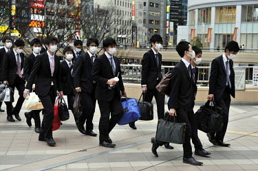 A group of young businessmen, all wearing surgical facemasks, approach the entrance to the Sendai Railway Station.