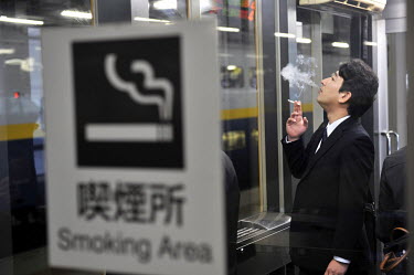 An office worker exhales the fumes from a cigarette in a smoking area on a platform at Sendai Railway Station.