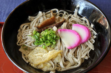 A bowl of Soba (buckwheat) noodles served with mushroom, scallions, beancurd and garish fish cake.