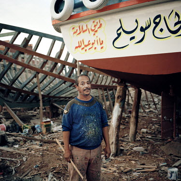 A sign painter, working in a dry dock 24.8 miles (40 km) south of the Suez canal, beside the Red Sea, stands in front of a boat which he has just finished working on. The Suez Canal connects the Medit...