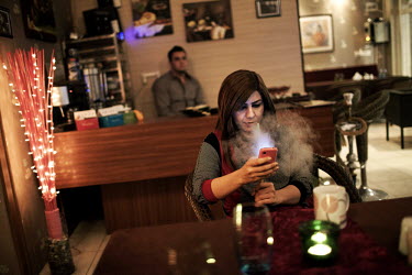A woman smokes a shish as she checks her mobile phone at a coffee shop.