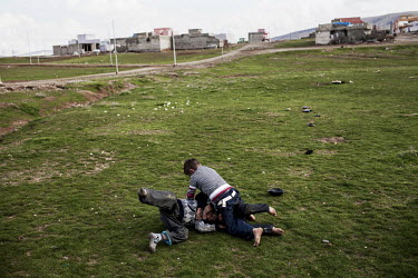Boys wrestle on the grass near their home.