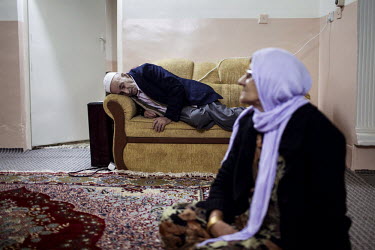 A woman sits on the floor as a man sleeps on a sofa at their home.