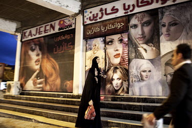 Women walk along a street past posters of models.