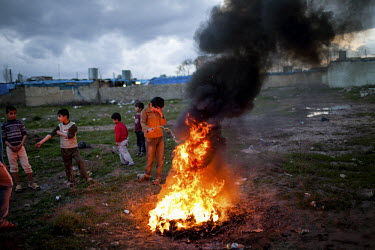 Children play by a fire, and black smoke rises from it.