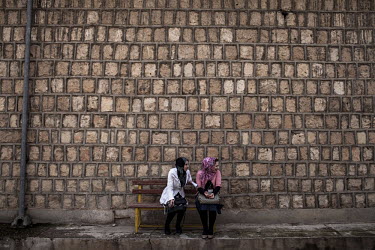 Women sit on a bench in front of a brick wall in the yeard of Duhok Polytechnic University.