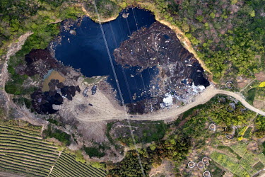 A pond contaminted with pollution, debris and garbage, next to traditional agricultural land.