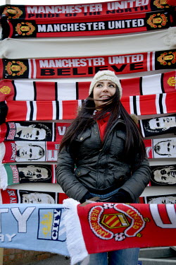A young woman sells Manchester United Football Club scarfs  outside Old Trafford prior to a Premier League match against local rivals Manchester City.