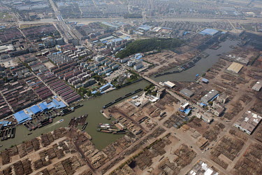 A canal divides a timber yard full of logs from an area containing housing and warehouses in the Jingangzhen district.