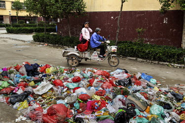 A woman drives her grandchild past a garbage heap at a housing project in Liaocheng city in the northeastern Chinese province of Shandong. They were all moved from their farmland and resettled nearby...