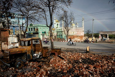 People drive past a burned out vehicle, damaged buildings and mosque, that was also damaged, in the Mingalar Zayyone Muslim quarter, that was razed by Buddhists in ethnic violence in March, in Meikhti...