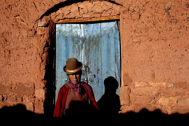 A woman stands in front of a blue door in Macha.   The people of Macha and surrounding communities carry on the pre-Columbian tradition of ritual fighting. The communities gather on the plaza of Macha...