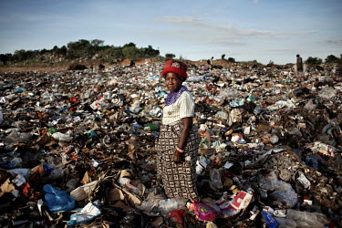 A woman stands among the detritus of a rubbish dump where she scavenges for items to recycle.