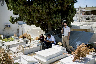 A man prays while a gunman looks on at a graveyard in Bab al-Tabbaneh during the funeral of 16 year old teenager. He was killed in a car bomb attack on the Taqwa Mosque on 23 August 2013.