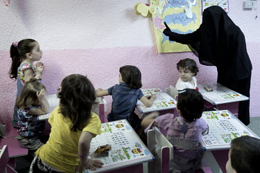A Koran class held in the basement of a house rented by a Kuwati businessman on behalf of Syrian widows and their children. The eldest refugee children enroll in local schools but the youngest are tau...
