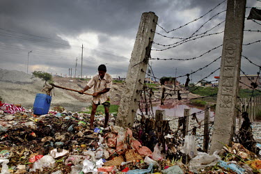 A man uses a tool to rake through a pile of rubbish as he searches for recyclable items.