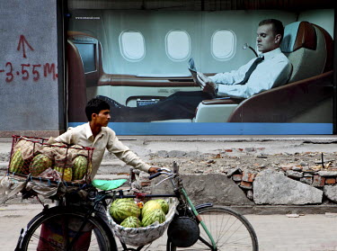 A man pushes his bicycle, loaded with melons, past a billboard advertisement for Oman Air's first class service.
