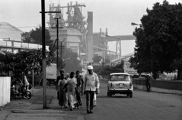 A steel worker walks along a road with the Tata Steel works dominating the background. This is the country's biggest and oldest steel works, employing some 26500 people.