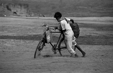 A man struggles through the sand with a bicycle loaded down by a sack of coal.