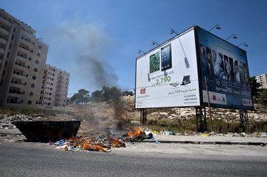 Uncollected rubbish burns in a street next to a billboard advertisement for the Apple iPad.