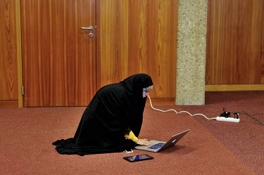 An Iranian state TV anchor woman wearing Islamic dress kneels on the ground, looking at her computer with a mobile phone and tablet lying next to the computer. She is one of the journalists attending...
