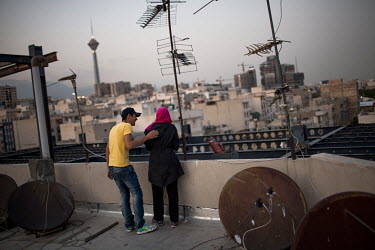A couple smoke on a roof, surrounded by satelites hidden from view from the ground as satelite televison is banned.