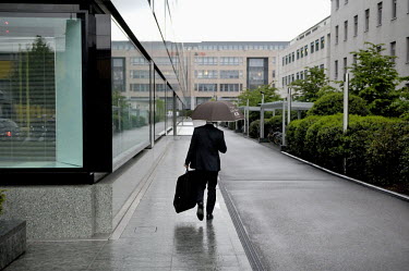A businessman, sheltering from the rain beneath an umbrella, walks to work in a newly developed banking quarter in the Acasias district. Pictet & Cie, private bankers are to the left and UBS at the en...