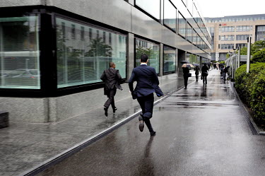 Businessmen, running from the rain, head to work in a newly developed banking quarter in the Acasias district. Pictet & Cie, private bankers are to the left and UBS at the end of the walkway.