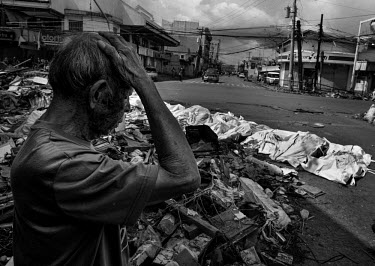 A man holds his hand to his head next to bodies of people killed in the typhoon which are laid out awaiting collection on an intersection in Tacloban City. Typhoon Haiyan, or Typhoon Yolanda as it is...