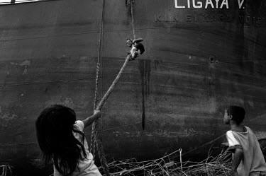 A boy climbs up a rope and two other children play on the ground next to a ship which has been washed ashore by the storm surge in Tacloban City. Typhoon Haiyan, or Typhoon Yolanda as it is known in t...