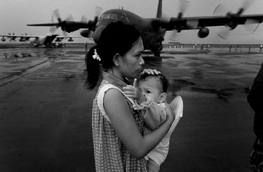 A woman holding a baby stands in a queue waiting to be evacuated to Manila or Cebu from the devastated town of Tacloban. US Army planes wait to take on passengers for the evacutation flight. Typhoon H...