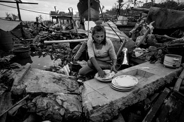 Helita Caruz Luchavez washes dishes in her makeshift shelter and the remains of her kitchen. 'Everything has been destroyed. Everything has gone. This is all we have been able to salvage in the rubble...