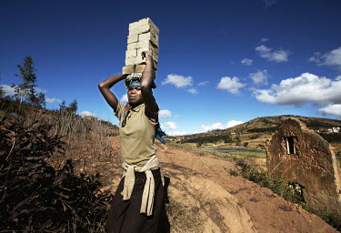 A woman carries a stack of bricks on her head up a hill to be fired in an oven.