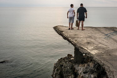 A man and a boy look over the black sea from a concrete platform.
