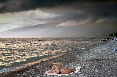 A man lies on a towel on the pebble beach at Gagra, the busiest seaside resort in Abkhazia. Dark clouds gather over the mountains in the distance.  Gagra is a mere 20 kilometres from the Russian borde...