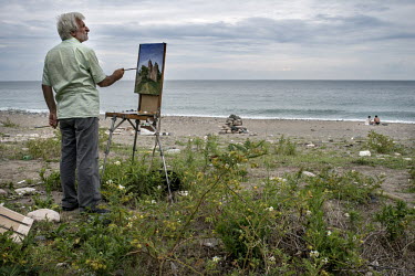 A local artist paints a wall and landscape near the beach in Sukhumi.
