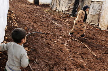 A woman walks across a muddy path past a young boy in a refugee camp for Syrian refugees in the Bekaa (Beqaa) Valley in Lebanon. Since the beginning of the civil war in Syria, some 880,000 Syrians hav...