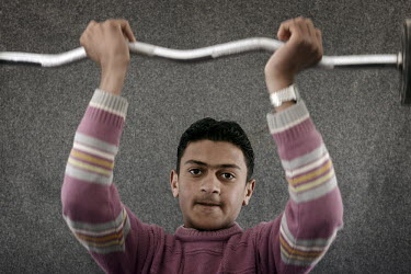 A young man using the weighlifting equipment in the Mens Activity Centre, set up by Save the Children, in the Za'atari refugee camp for refugees who have fled the fighting in neighbouring Syria. In Ju...